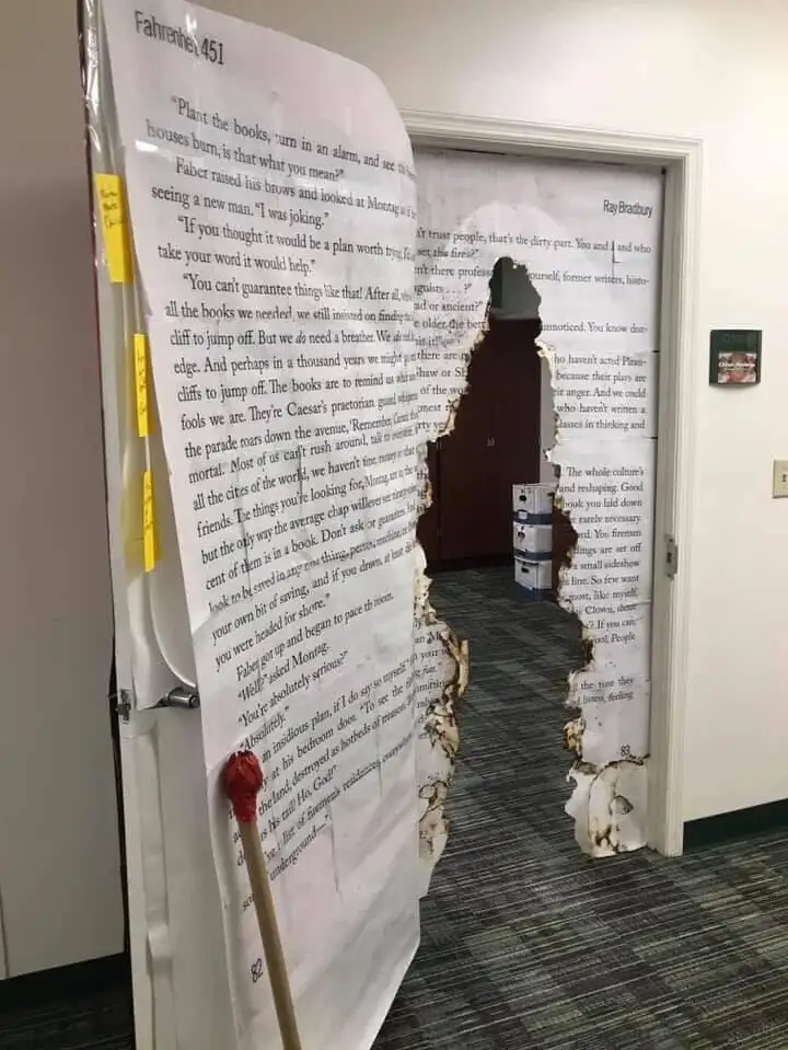 A doorway is covered in large printed pages of text from Ray Bradbury's Fahrenheit 451, with a torn hole revealing a dark…