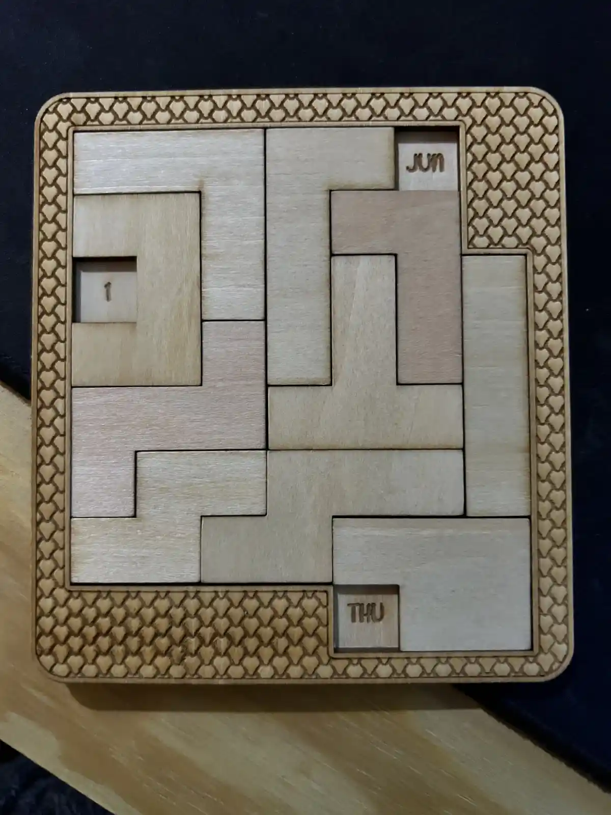 A wooden puzzle with interlocking pieces arranged to form a grid, featuring a small square piece labeled '1' in the top-left…