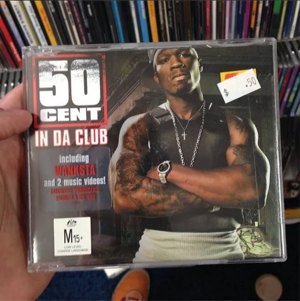 A hand holds a CD case for 50 Cent's album 'In Da Club', featuring the artist with tattoos and a watch, arms crossed. The…
