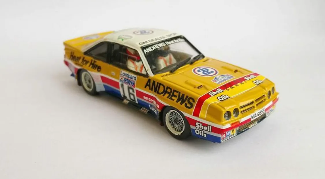 A yellow, red, and blue scale model of a vintage rally car with sponsor decals including 'Shell Oils', 'Michelin', and…
