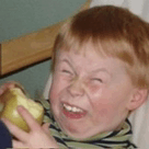 A young child with red hair and a striped shirt is holding an apple, making a comically exaggerated crying face with eyes…