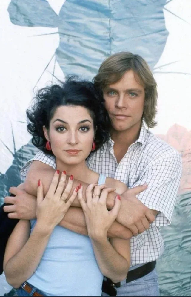 A man and woman are posed closely together in a vintage photo, the man has his arms wrapped around the woman from behind…