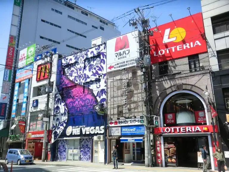 A street view in Japan shows a building with a large purple and white damask-patterned mural advertising 'SLOT GATE NE…