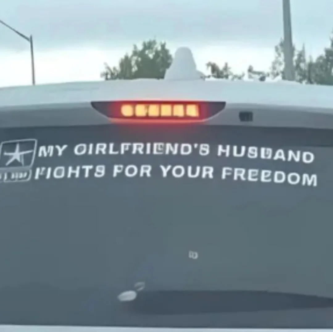 The rear of a dark-colored vehicle, likely a truck, is shown with a white decal on the back window. The decal features a…