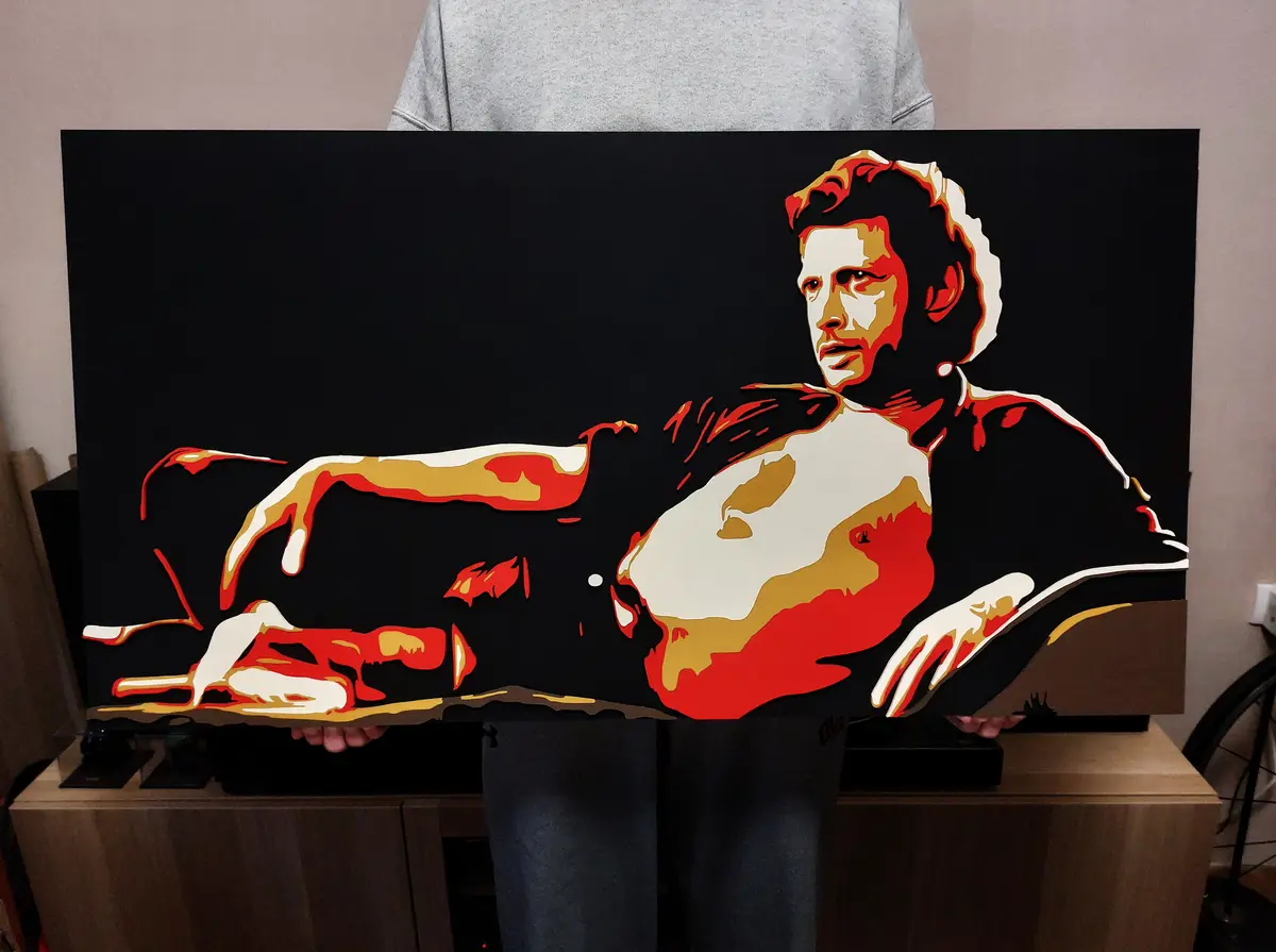 A person holds up a large, stylized painting depicting a man in a reclining pose, rendered in bold red, white, and gold…