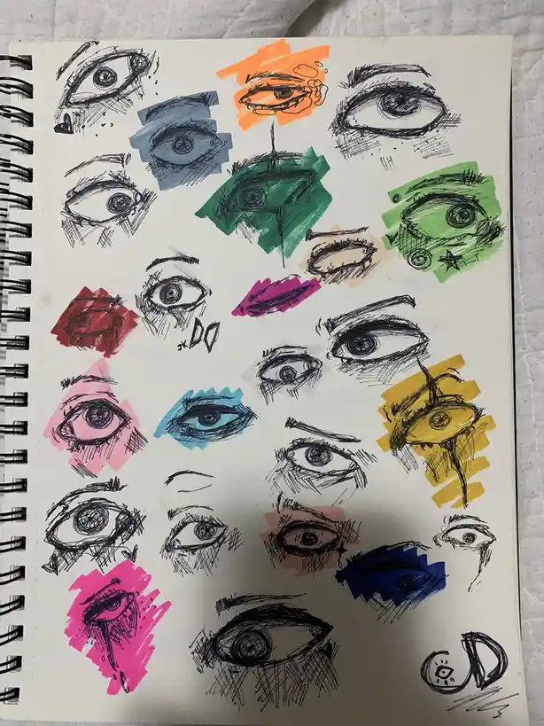 A spiral-bound sketchbook page filled with numerous hand-drawn eye sketches, each colored with different markers in vibrant…