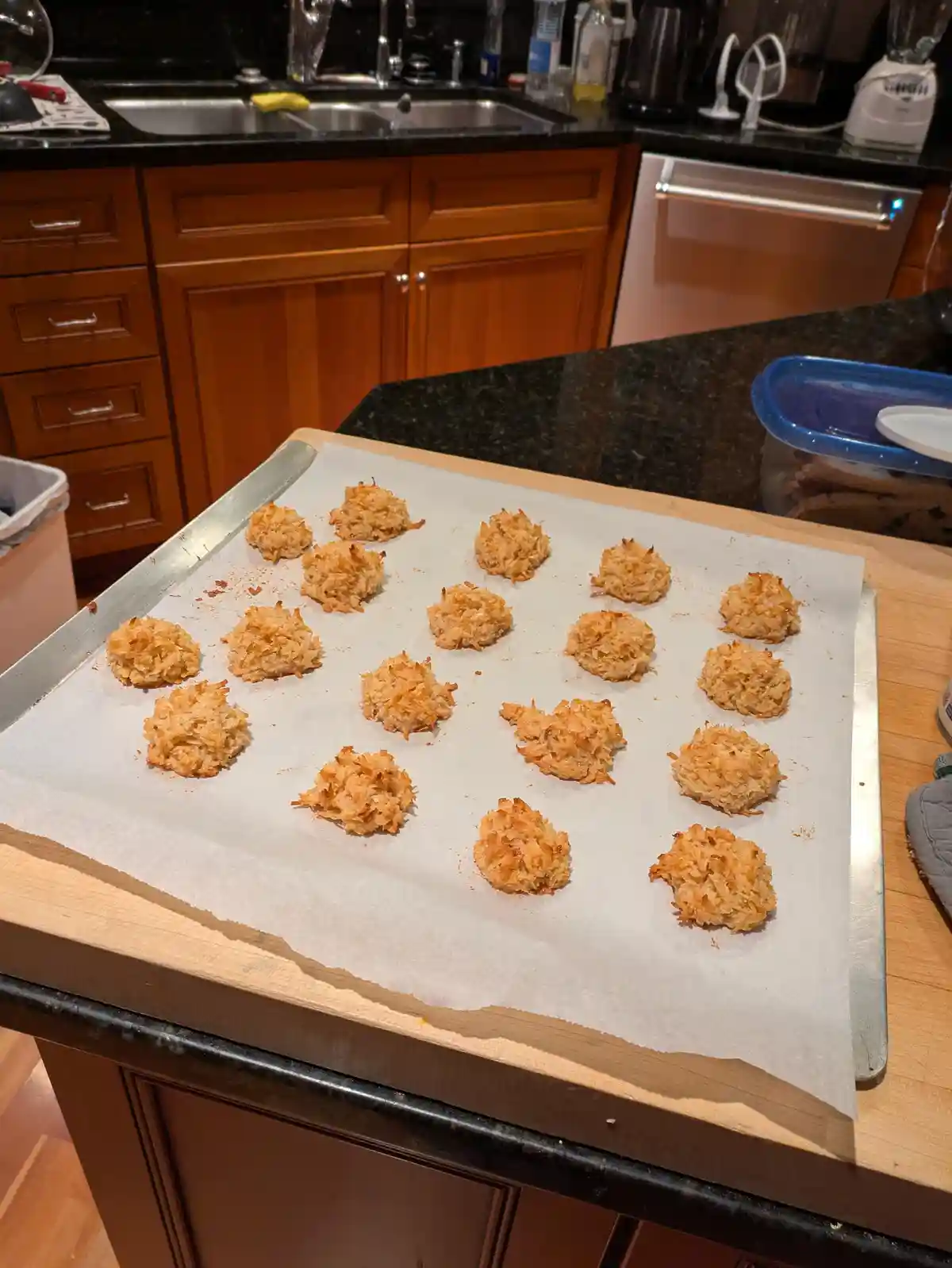 A baking sheet lined with parchment paper holds about twenty golden-brown, slightly unevenly shaped coconut macaroons on a…