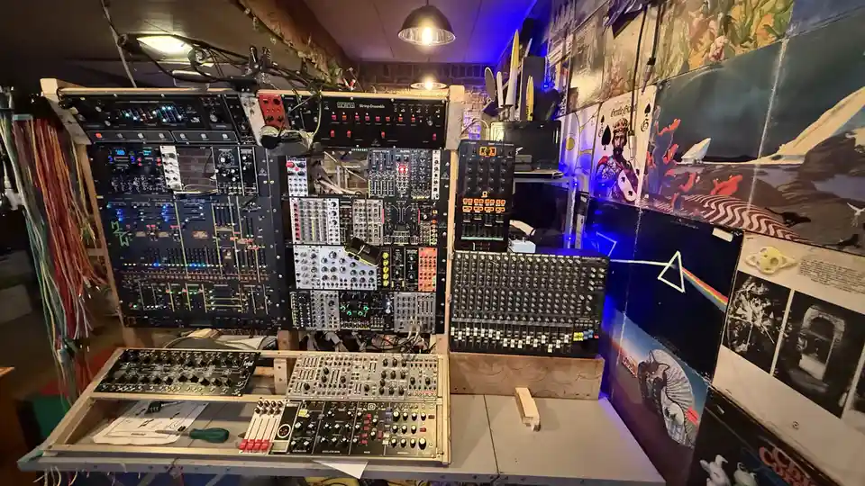 A densely packed, custom-built modular synthesizer setup with numerous black and silver modules, knobs, and illuminated…