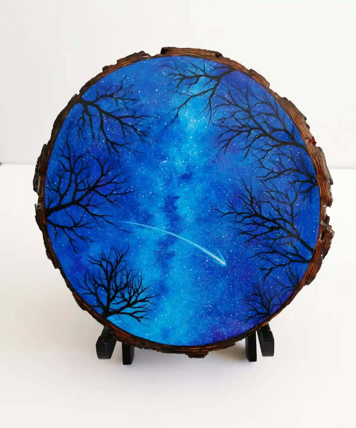 A circular wooden slice with a rough, natural bark edge is displayed on a black stand against a white background. The…