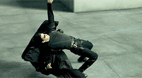Six sequential frames show two men in black suits performing a synchronized, slow-motion, acrobatic flip across a concrete…