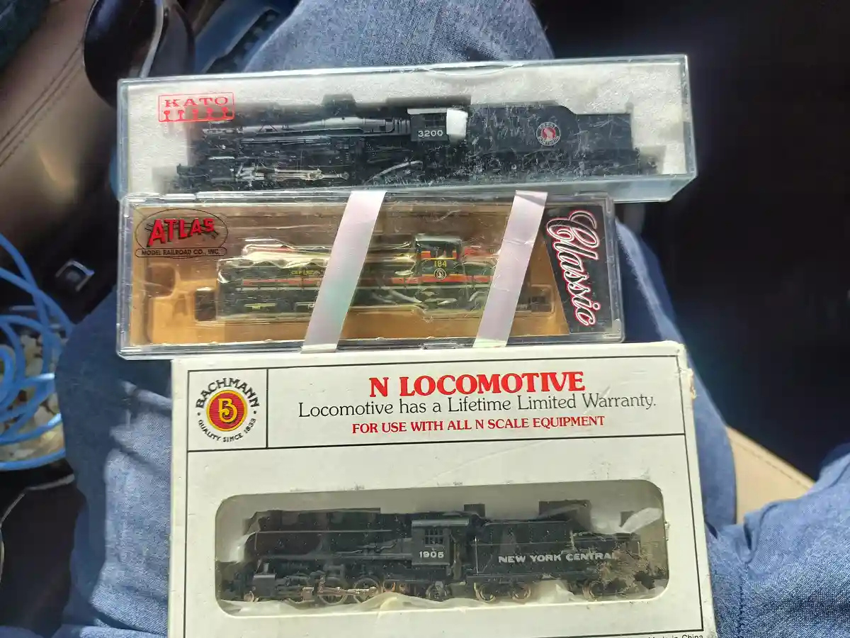 Three model train boxes are stacked, showing N-scale locomotives from Kato, Atlas, and Bachmann. The bottom Bachmann box has…