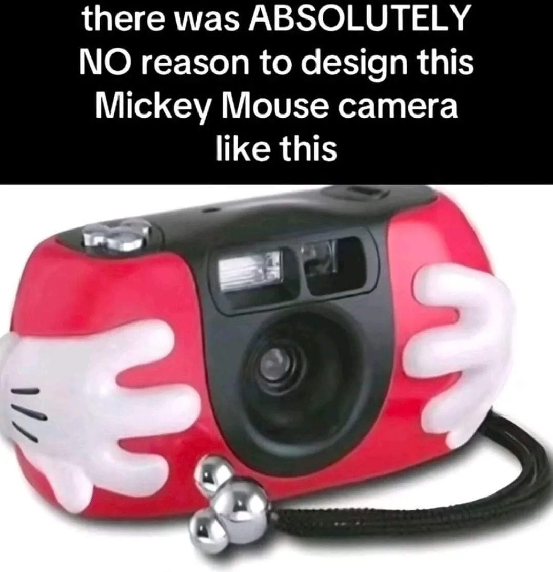 A red and black Mickey Mouse-themed camera with white gloved hands on either side and a silver bell-shaped strap, overlaid…