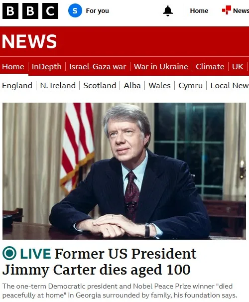 A BBC News screenshot shows a photo of former US President Jimmy Carter seated at a desk with an American flag behind him…
