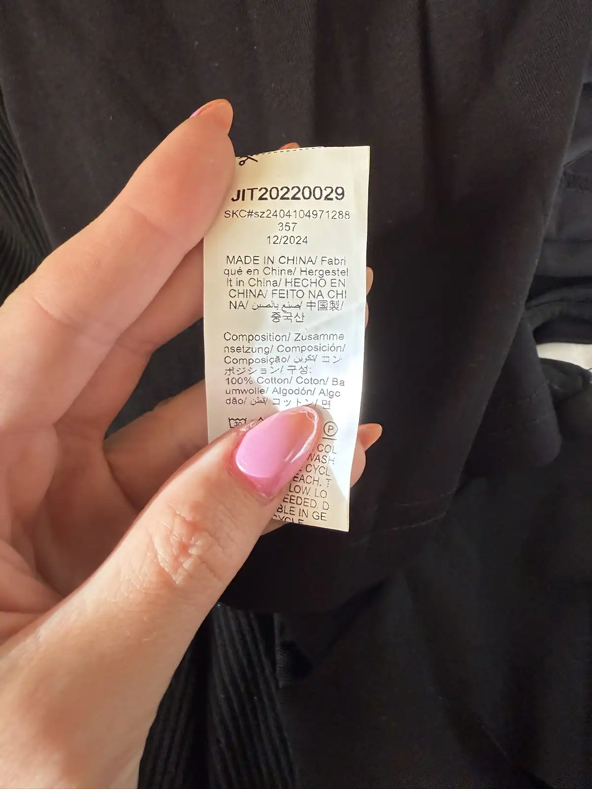 A hand with pink nail polish holds up a clothing care label that repeatedly states 'MADE IN CHINA' in multiple languages…