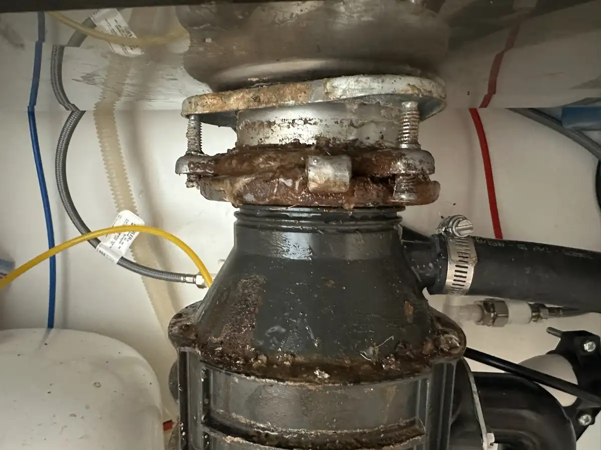 A close-up photo shows a heavily clogged and grimy garbage disposal unit under a sink, with thick brown gunk and food debris…