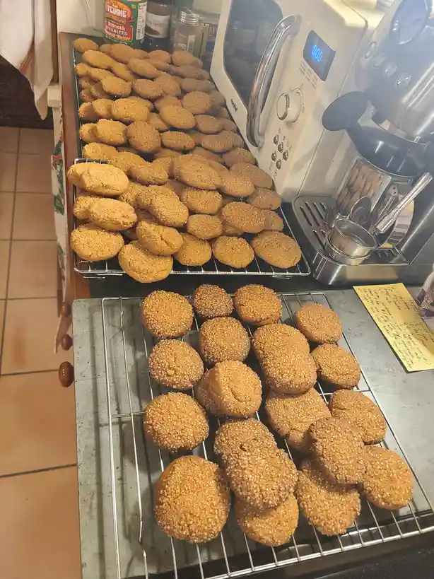 Three tiers of cooling racks are filled with freshly baked, golden-brown cookies, each tier showing a different texture or…