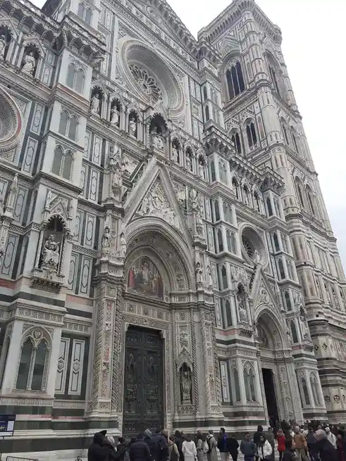 A low-angle photo shows the ornate, multi-colored facade of Florence's Cathedral (Duomo), crowded with tourists at its base…