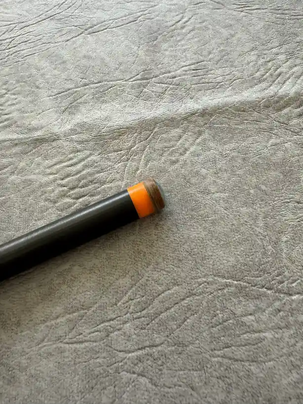 A close-up photo shows the tip of a black cylindrical object, likely a pen or marker, resting on a textured gray surface…