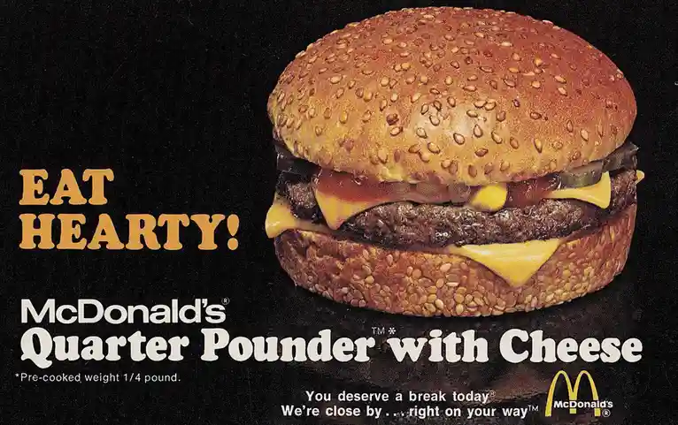 A vintage McDonald's advertisement featuring a large, sesame-seeded burger with a beef patty, melted cheese, and pickles…