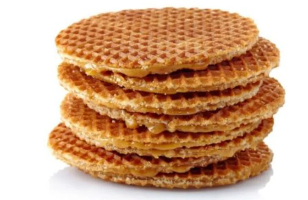 A stack of seven round, golden-brown waffle cookies with caramel filling visible between layers, set against a plain white…
