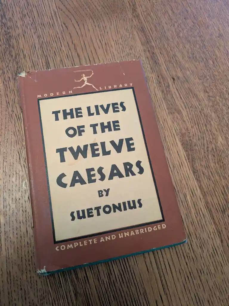 A vintage brown hardcover book titled 'The Lives of the Twelve Caesars' by Suetonius, part of the Modern Library series…
