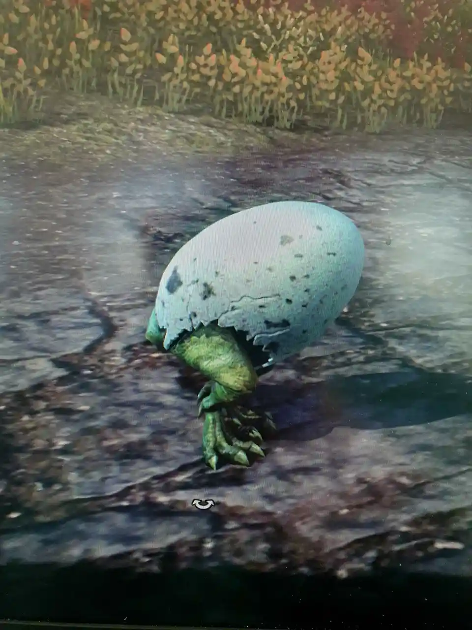A large, speckled egg with a green, scaly dinosaur-like foot and clawed foot emerging from its cracked shell, set on a rocky…