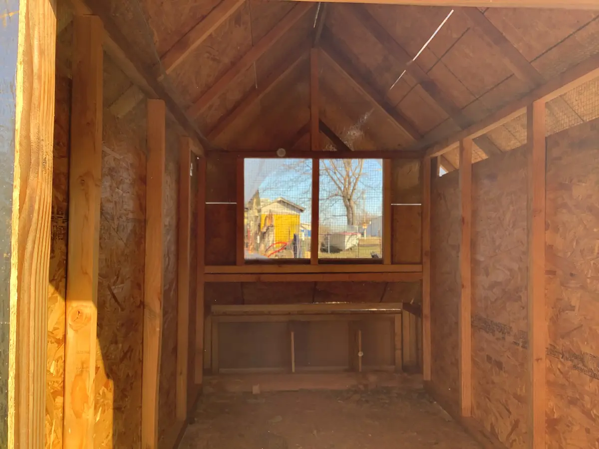 The image shows the interior of a wooden structure under construction, likely a chicken coop, with exposed OSB walls, wooden…