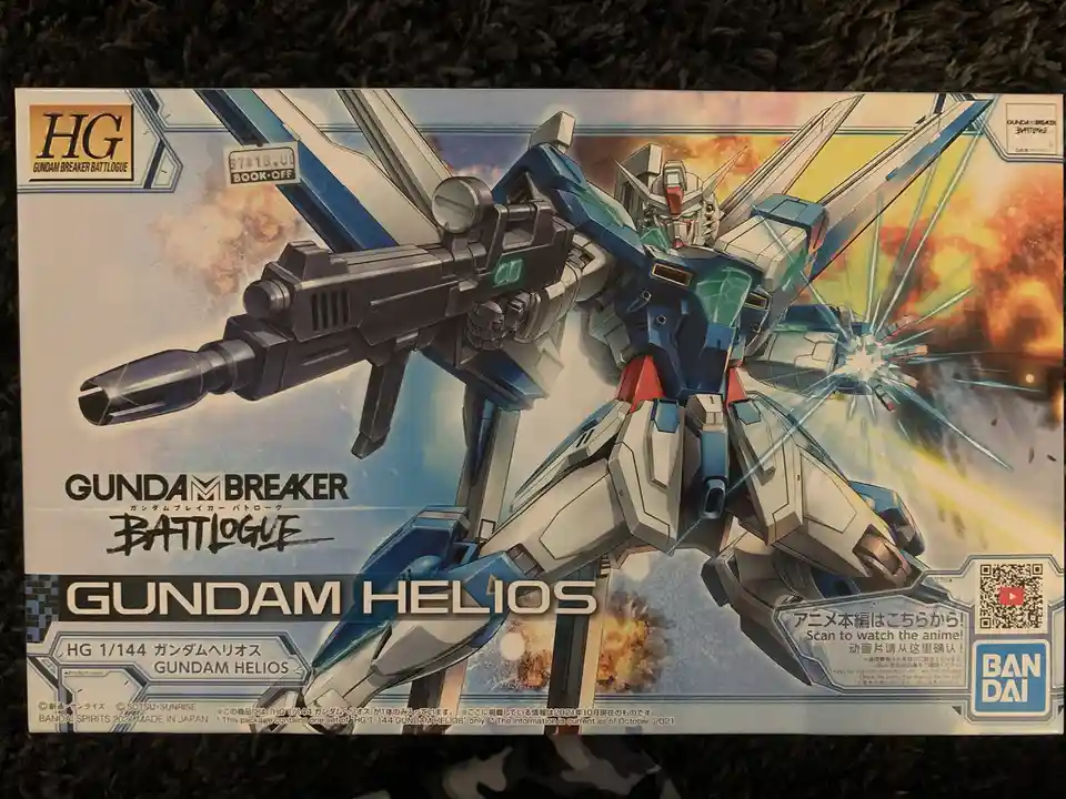 A photo of a Bandai HG 1/144 scale model kit box for Gundam Helios from the Gundam Breaker Battlogue series. The box art…