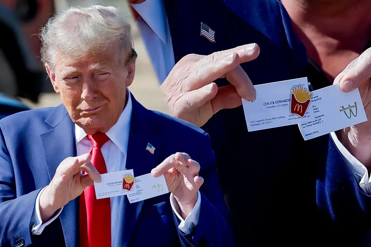 A man in a blue suit and red tie holds two business cards that have been altered to feature McDonald's logos instead of his…