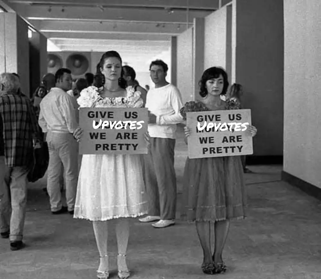 Two women in vintage dresses hold identical signs reading 'GIVE US UPVOTES WE ARE PRETTY' in a black-and-white photo of a…