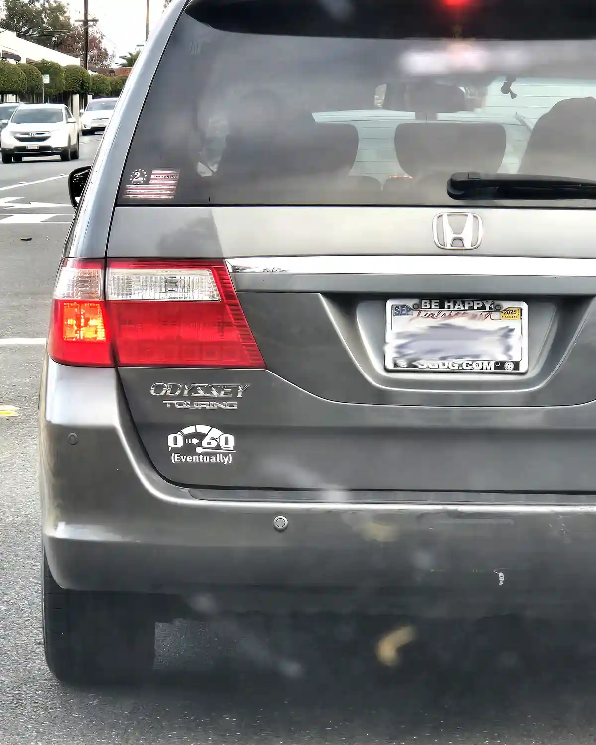 The rear of a silver Honda Odyssey Touring minivan is shown, featuring a sticker that reads '0-60 (Eventually)' below the…