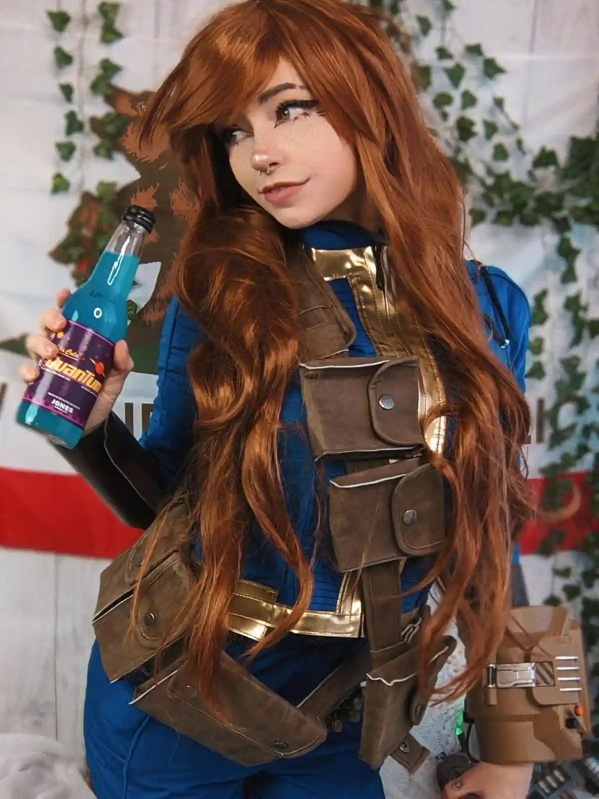 A person in a detailed cosplay of a character with long reddish-brown hair, wearing a blue jumpsuit with brown utility gear…