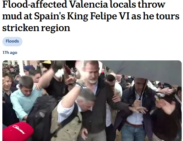 A news article screenshot shows a crowd of people, some holding umbrellas, surrounding a man in a dark jacket who appears to…