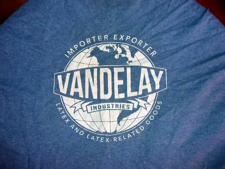 A close-up of a blue t-shirt featuring a white circular logo with a globe design. The logo reads 'IMPORTER EXPORTER' at the…