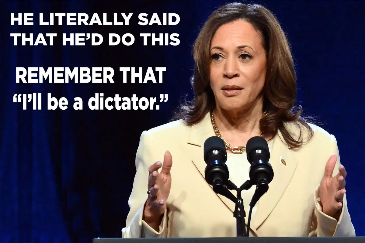 A woman in a light-colored suit stands at a podium with two microphones, gesturing with both hands while speaking. Large…