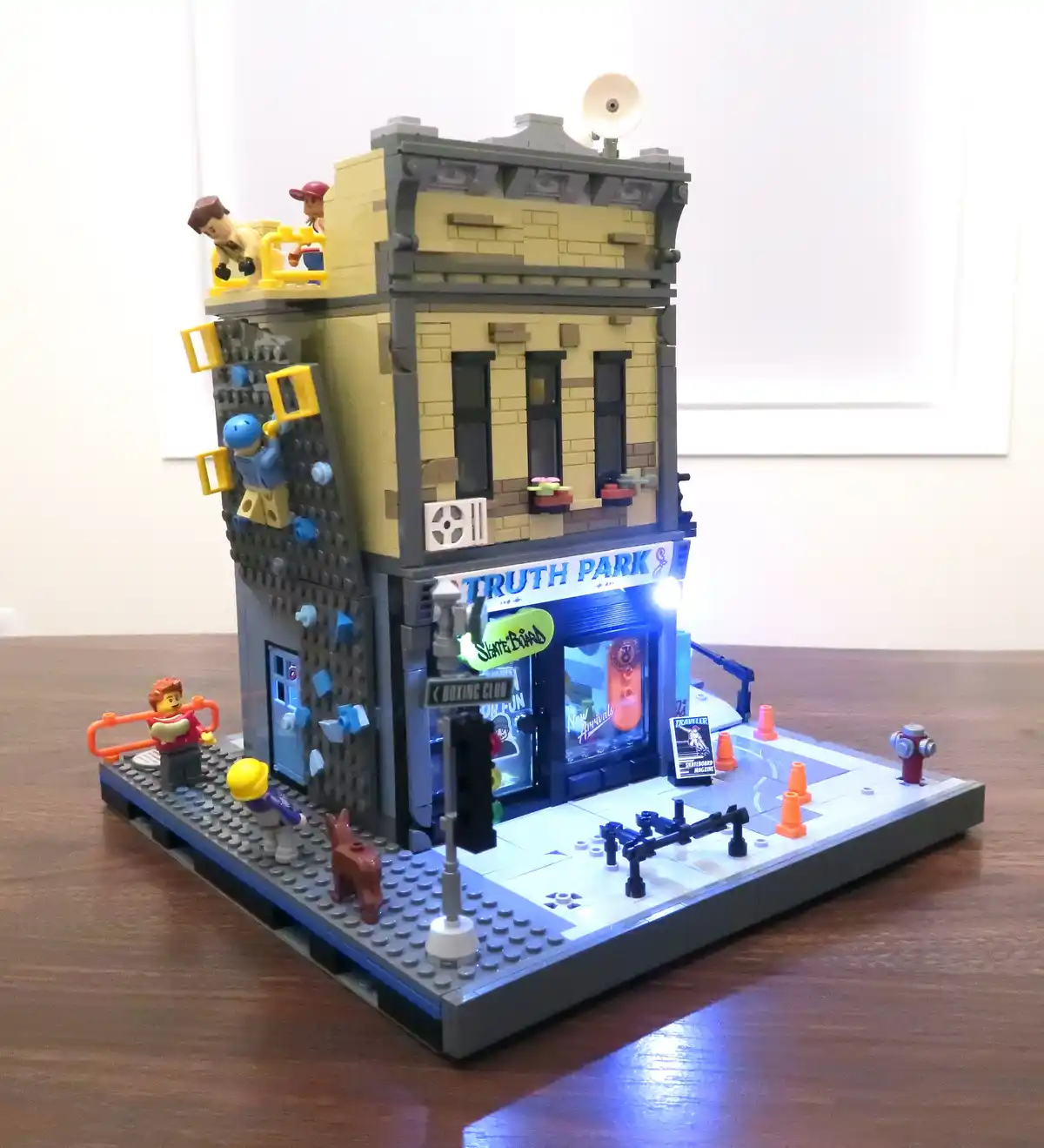 A detailed LEGO model of a two-story building labeled 'TRUTH PARK' with a lit storefront, climbing wall, and minifigures on…