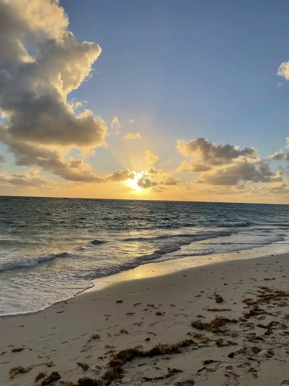 A serene beach sunset photo with golden sun rays breaking through clouds over the ocean, casting light on gentle waves and…