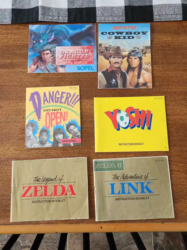 Six vintage NES instruction booklets are laid out on a wooden table with a checkered cloth above. The booklets include…