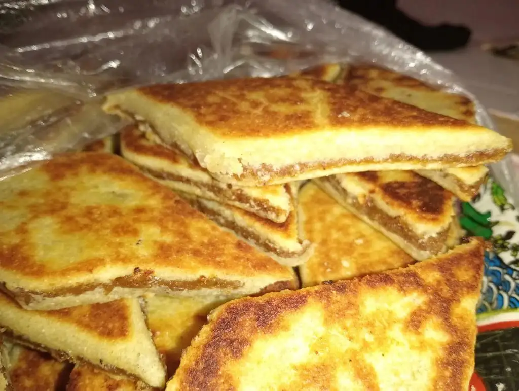 A close-up photo shows a pile of golden-brown, triangular toast sandwiches stacked on a patterned plate, with a plastic bag…