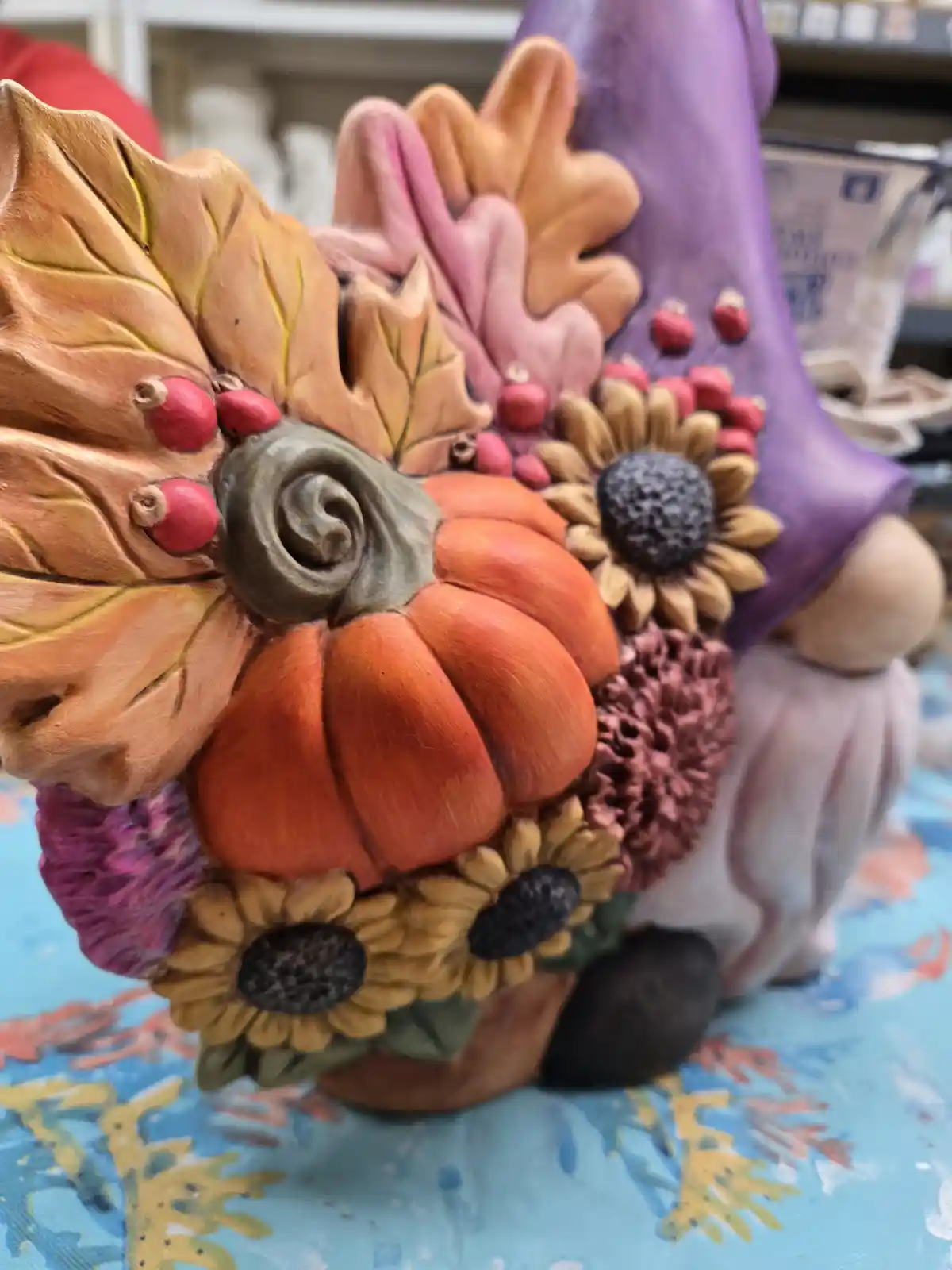 A close-up of a decorative garden gnome with a purple hat and white beard, whose head is entirely covered in autumn-themed…