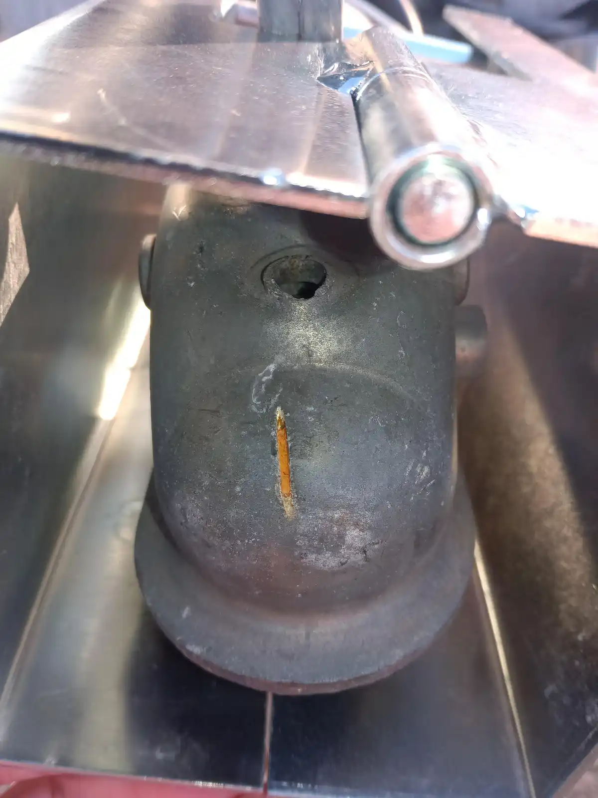A close-up photo shows a dark, worn metal object resembling a face, with a rusted vertical line for a mouth and a hole for…