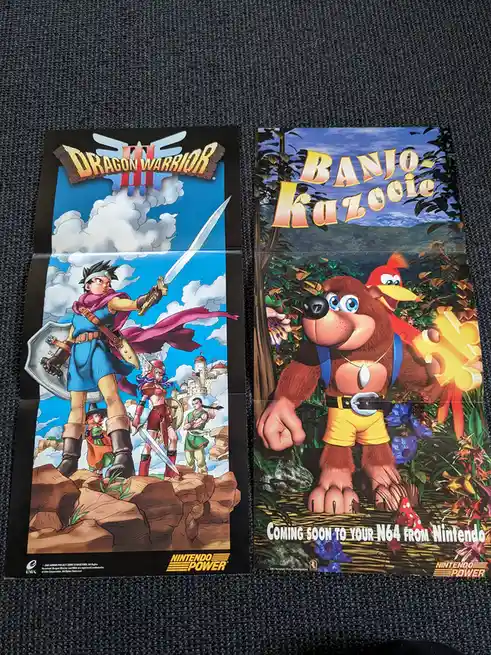 Two folded Nintendo Power promotional posters lie side by side on a dark carpet. The left poster features the game Dragon…