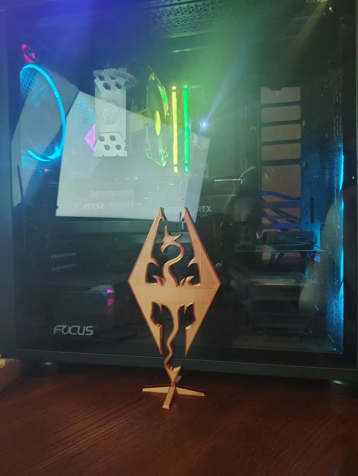 A custom-built PC with a glass case, illuminated by blue and green RGB lights, sits on a wooden surface. In front of it is a…