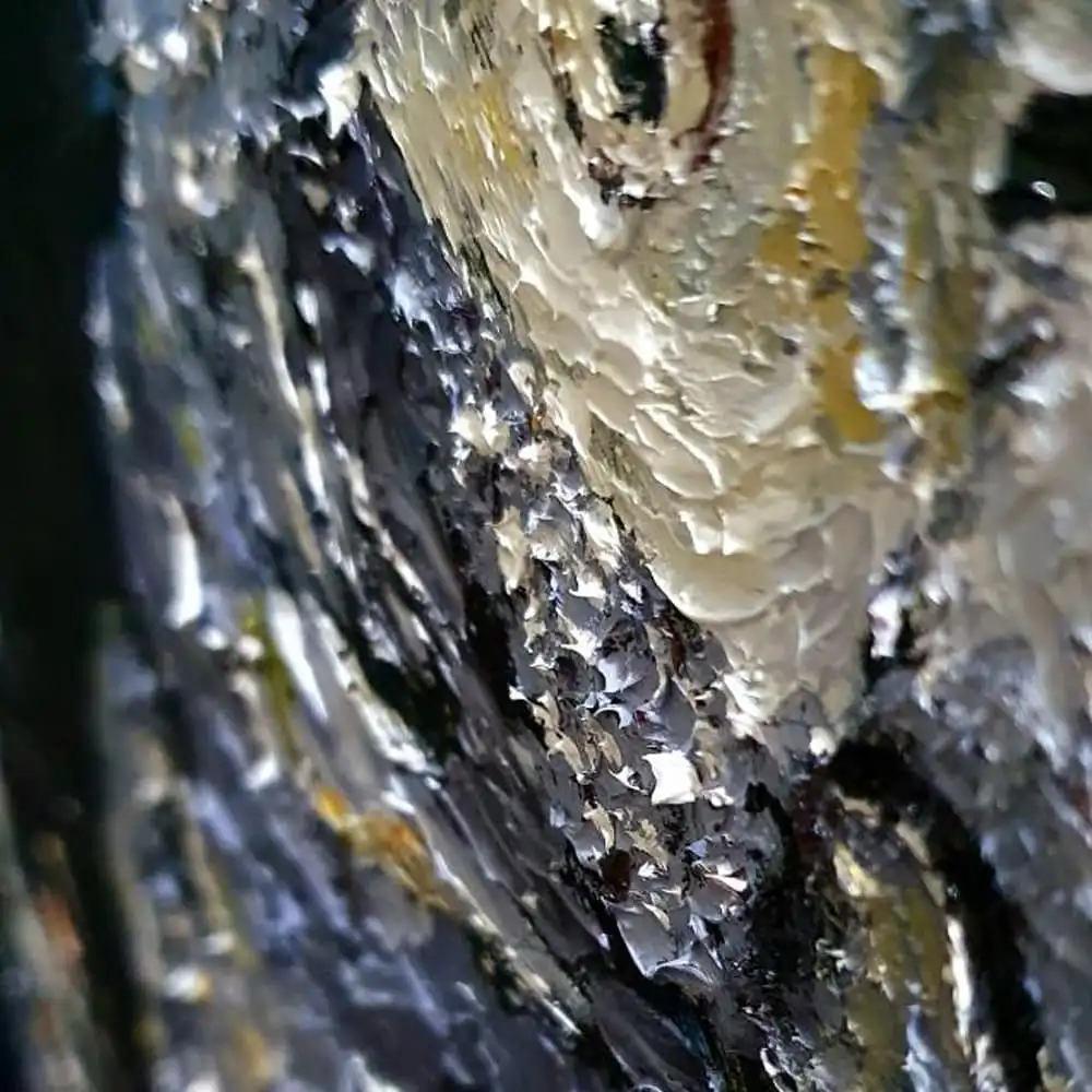 A close-up photo of textured, layered paint with thick, glossy, and cracked white and gray strokes over darker tones…