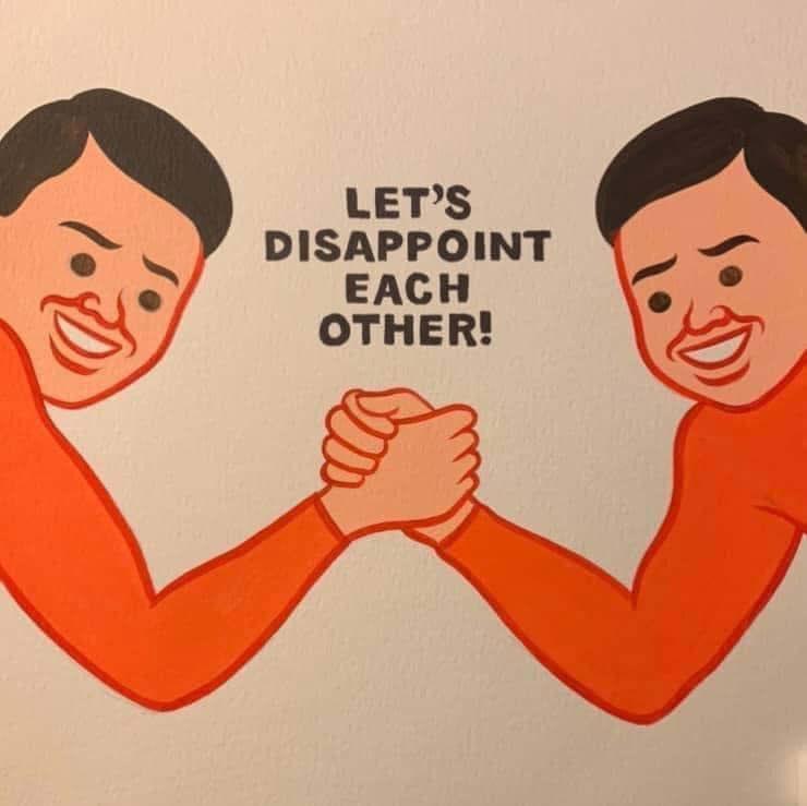 Two cartoon men with exaggerated smiles and clenched fists are arm wrestling against each other. The text overlaid in the…