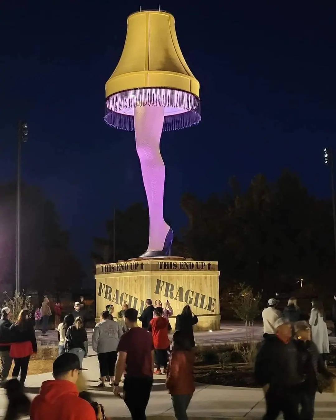A giant statue of the iconic 'A Nightmare on Elm Street' leg lamp, featuring a yellow lampshade with purple fringe and a…