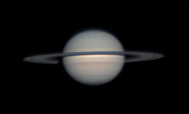 A blurry, low-resolution image of the planet Saturn with its iconic rings against a black background. Overlaid text in white…