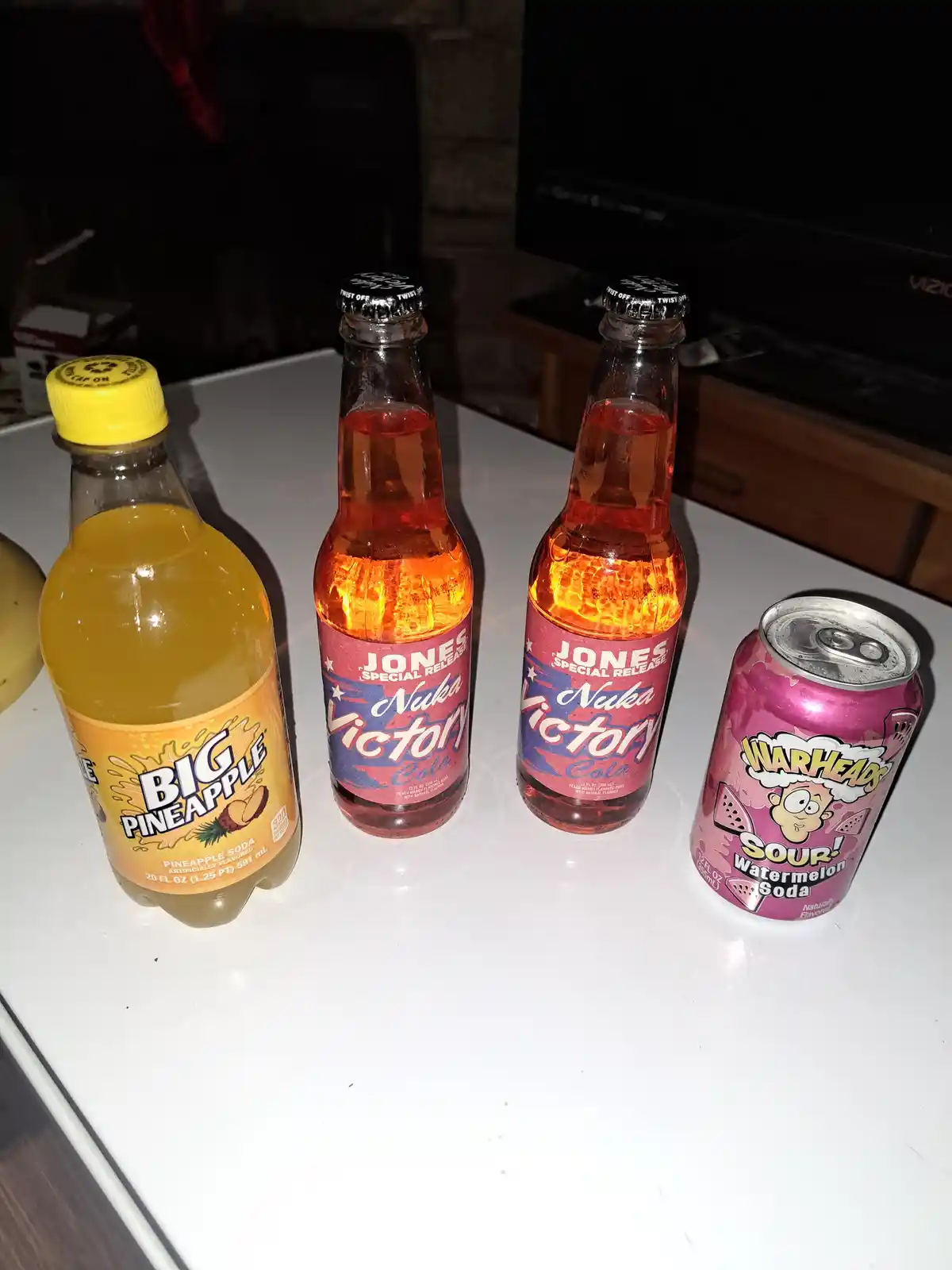 Four beverages sit on a white surface: a yellow-labeled 'Big Pineapple' soda bottle, two identical 'Jones Special Release…