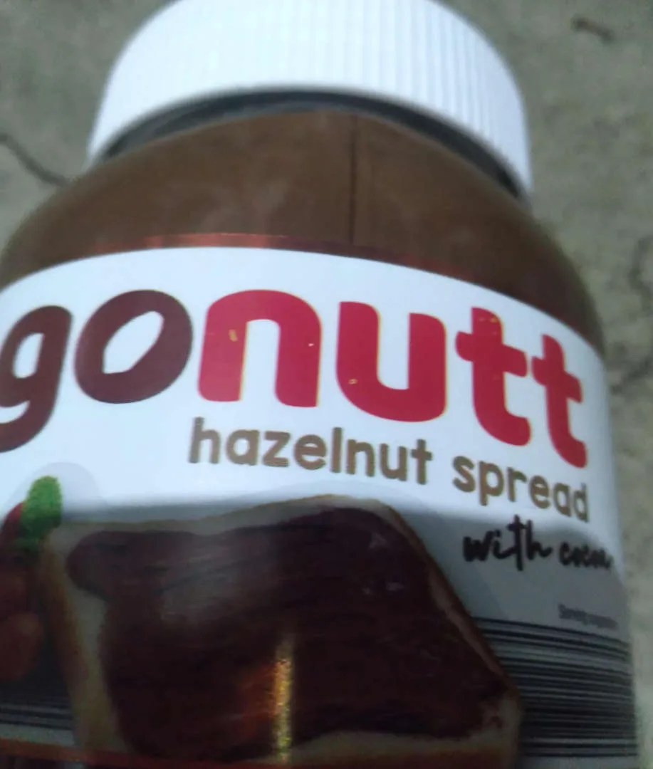 A close-up photo of a jar of hazelnut spread with a white lid, where the brand name is altered to read 'gonutt' by changing…