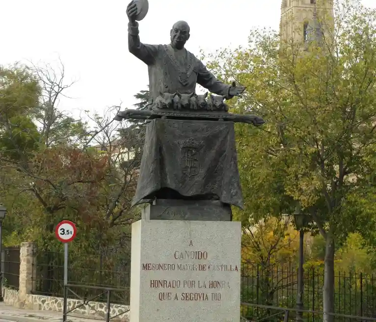 A bronze statue of a man in formal attire, holding a hat aloft and gesturing with his other hand, stands atop a pedestal…